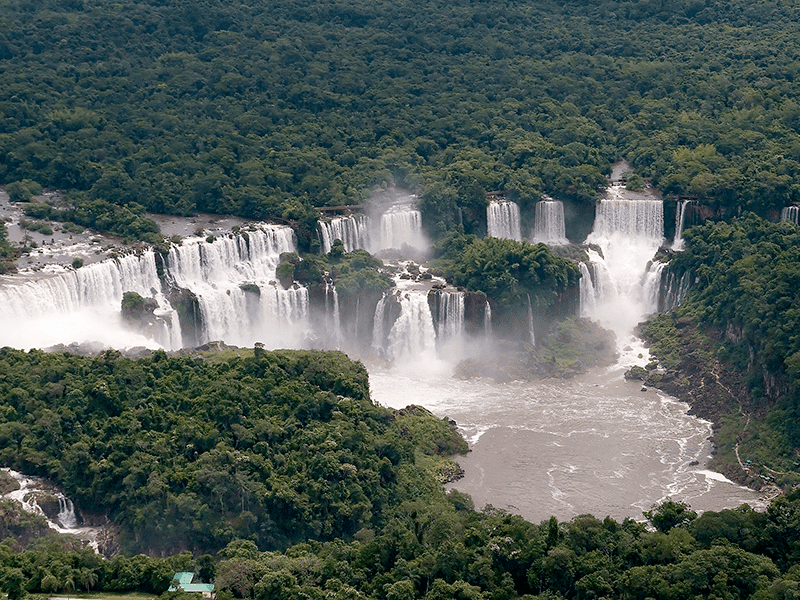 Vista aérea das Cataratas do Iguaçu com várias quedas d'água rodeadas por uma densa floresta.