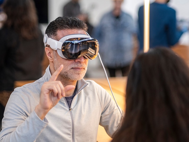 A foto mostra um homem vestido com uma camisa cinza, realizando gestos e vestindo o seu Apple Vision Pro.