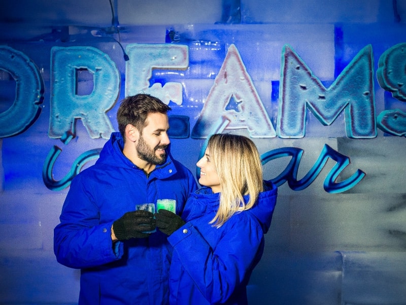 A foto mostra um casal vestido de azul, eles estão brindando com copos de gelo no Dream Ice Bar.