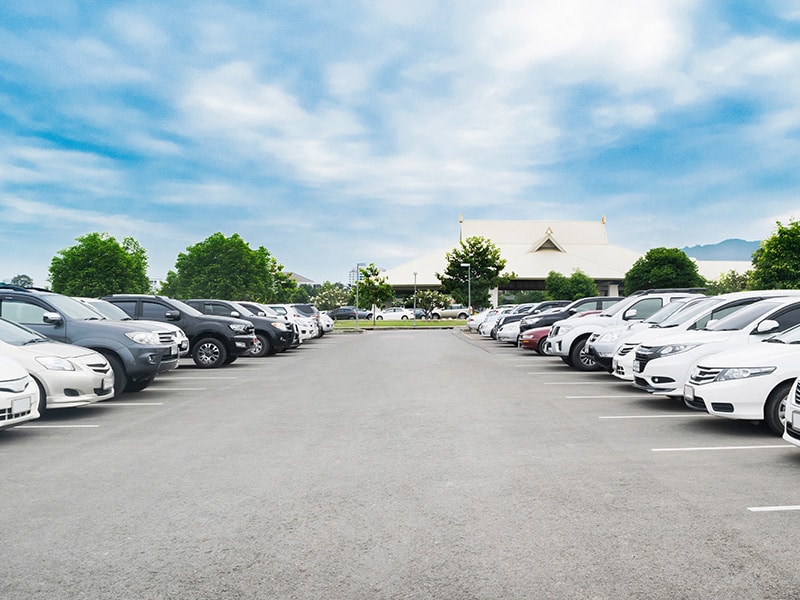 A foto mostra um estacionamento com vários carros parados em ambos os lados.