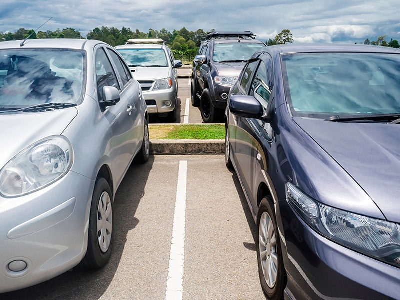 A foto mostra de perto alguns carros estacionados em um estacionamento.