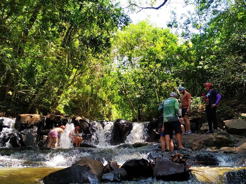 A foto mostra as pessoas em um rio com pequenas cachoeiras.