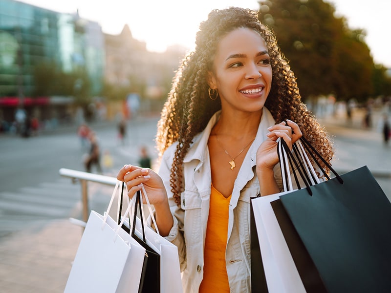 A foto mostra uma mulher segurando várias sacolas de compras