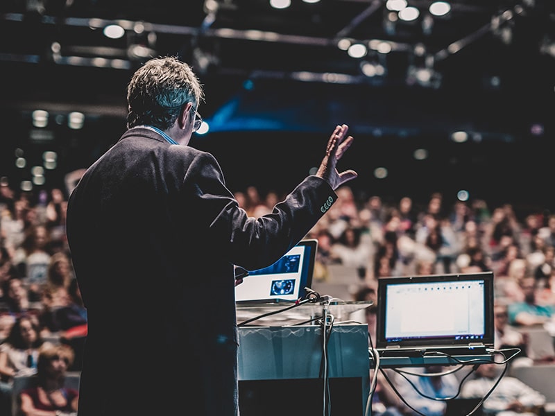 A foto mostra um palestrante no palco com várias pessoas assistindo, assim como será no Sindepat em Foz 2024.